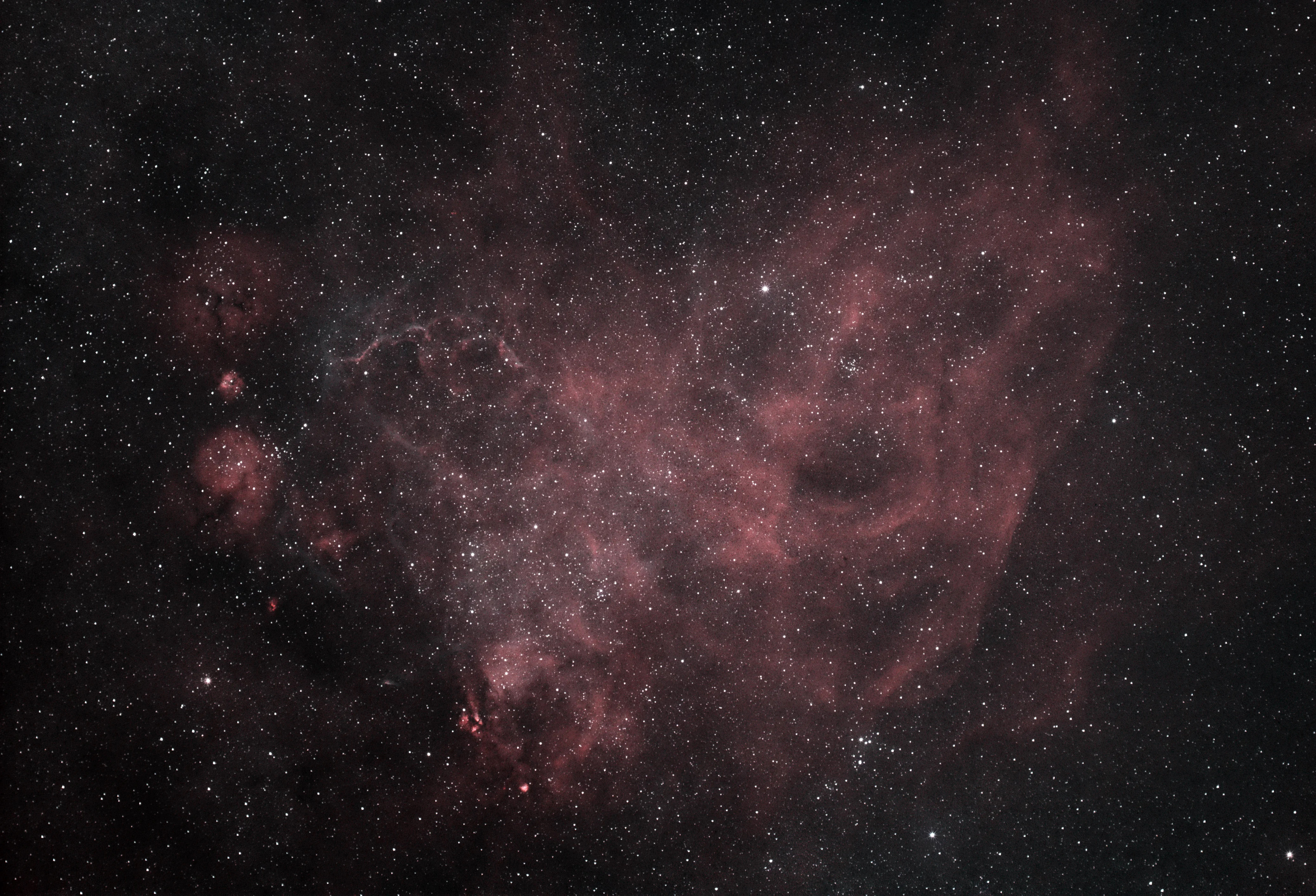 A textured pink blob on a dark starry background. There are a few small brighter patches, which have stars if groups of stars embedded in them. 

Left of center, there is some frondy structure. 