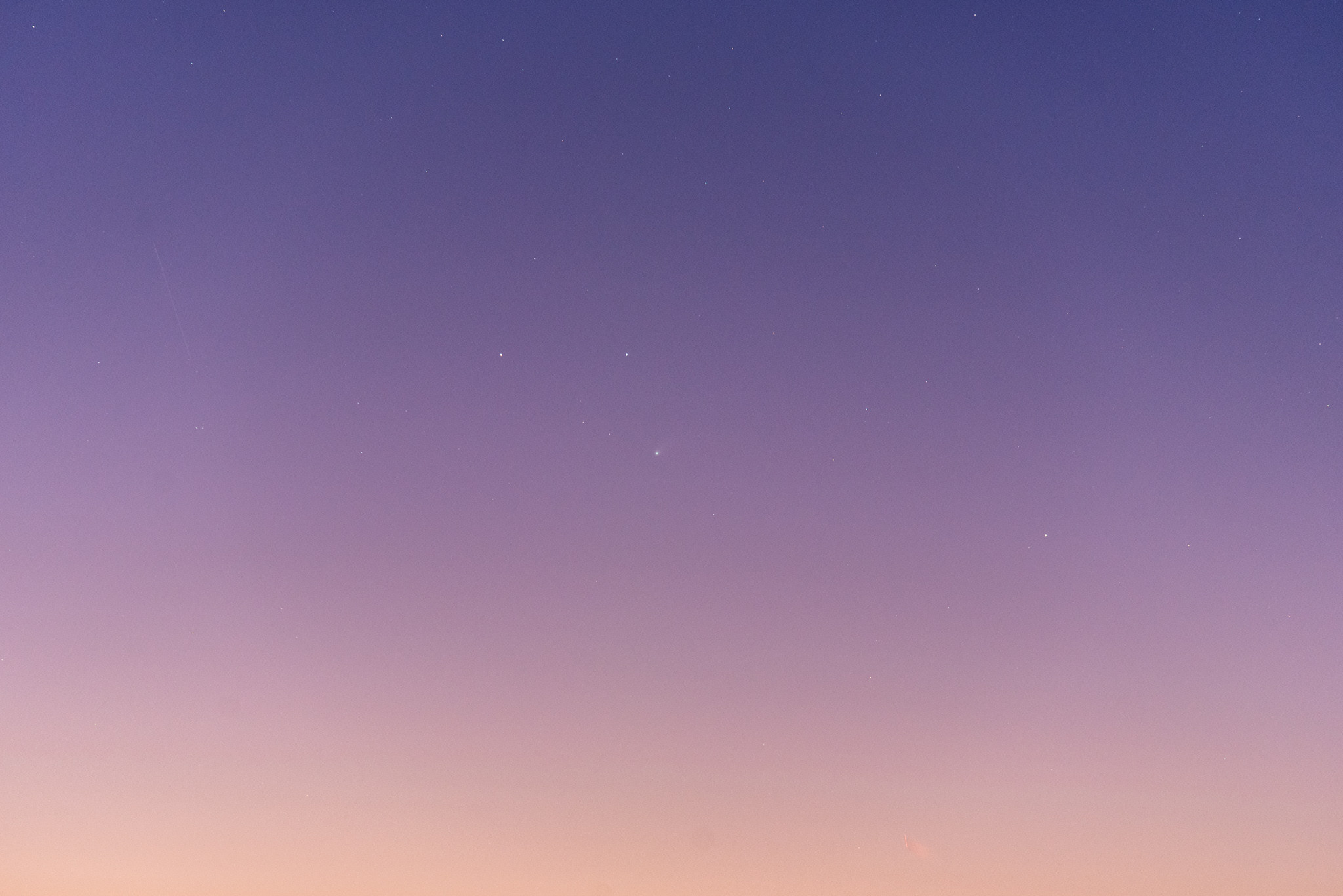 A sunset gradient sky, salmon pink at bottom and faintly purple at the top. A few stars are scattered around and at center is a faint fuzzy blob. 