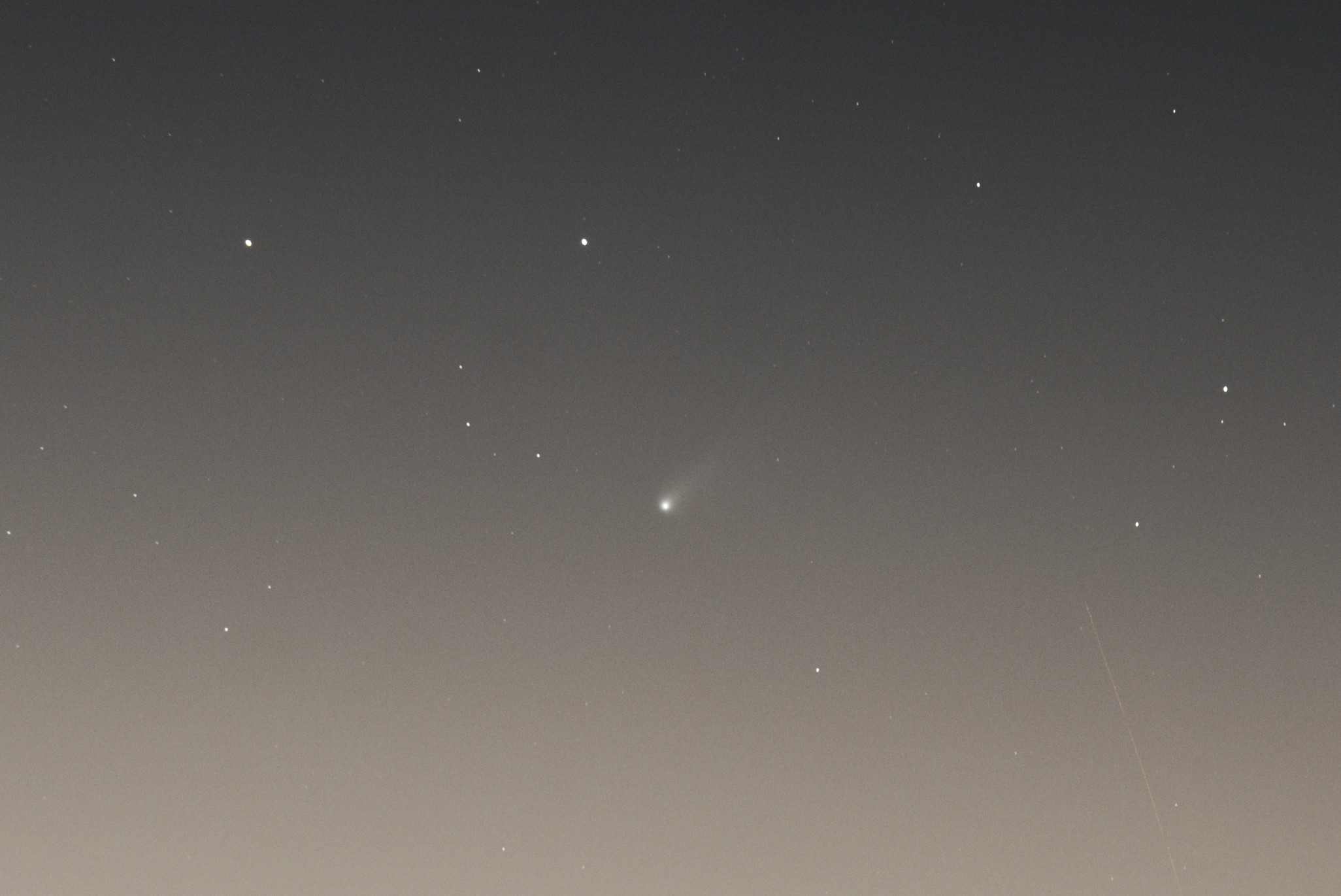 A sunset gradient sky with a handful of tiny bright stars and in the middle a fairly bright fuzzy dot with a faint tail pointing towards the top right. 